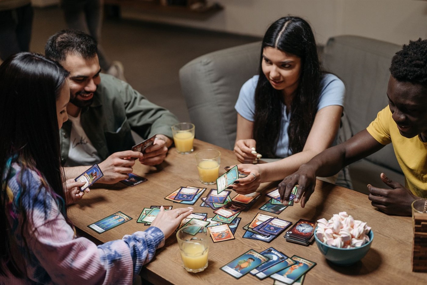 Four friends sitting around a table playing a card game together in daylight